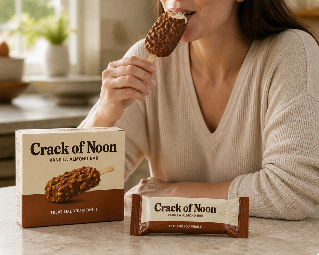 Person holding a Crack of Noon concept frozen bar with the carton and wrapper on a kitchen counter.
